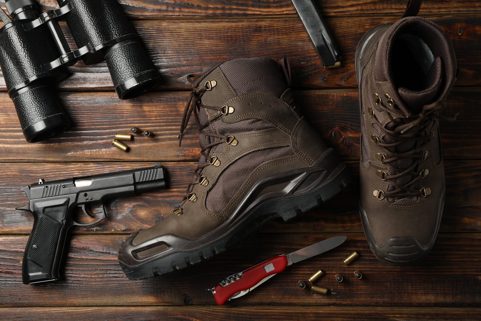 Pair of brown leather tactical boots on a wooden surface, with binoculars, a pistol and cartridges
