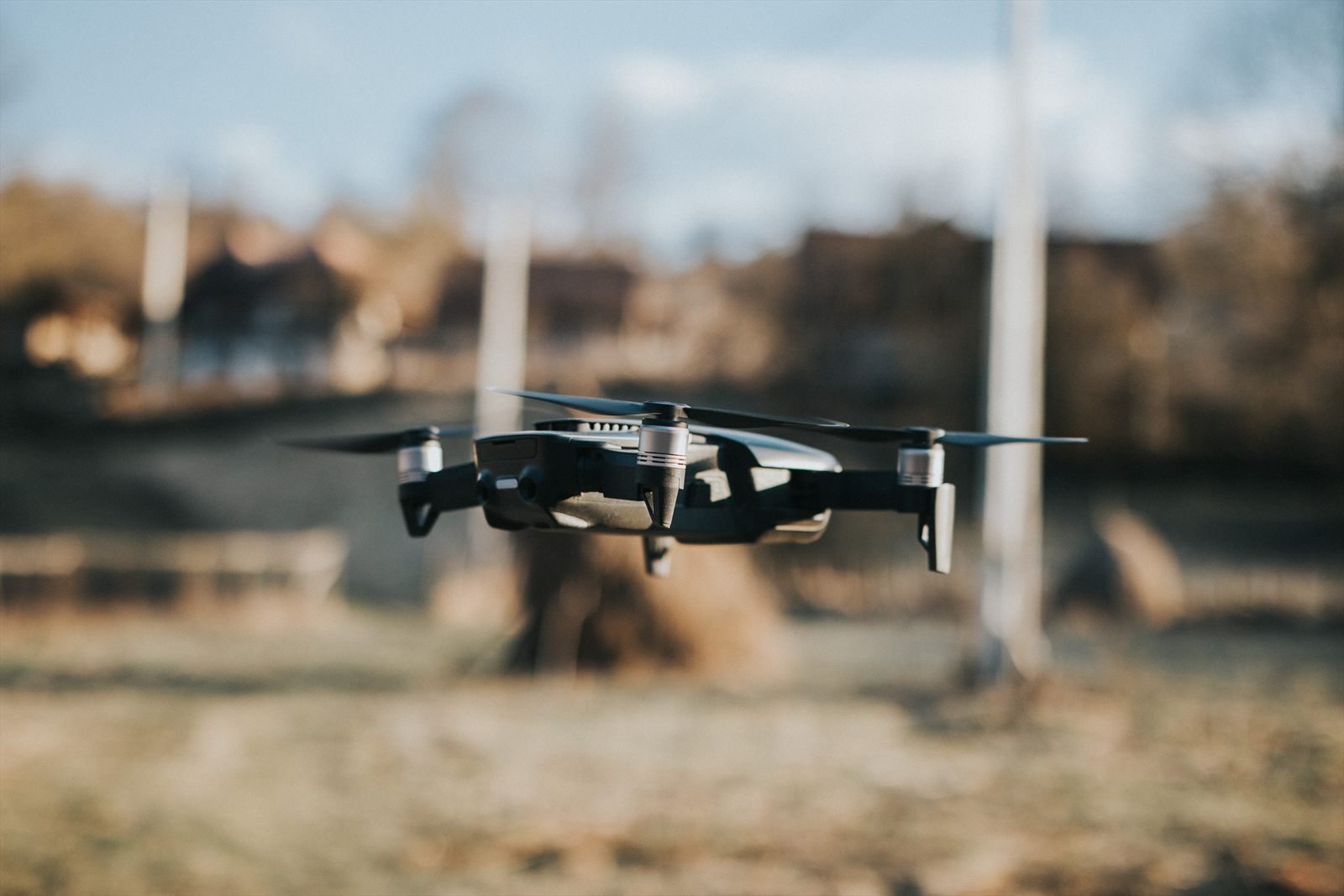 Small folding quadcopter drone hovering in flight over open ground