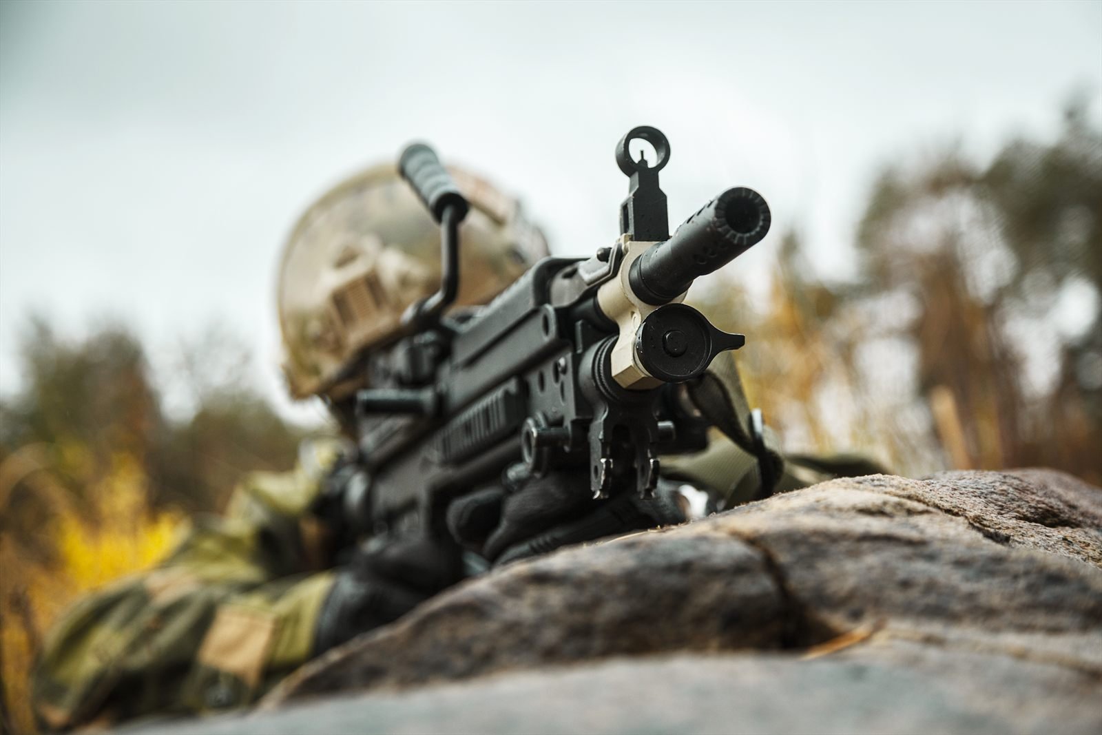Soldier in a prone firing position behind a service rifle on rocky ground